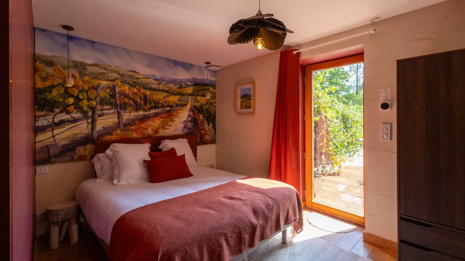 Chambre avec un lit double, une porte vitrée donnant sur une terrasse et une peinture murale représentant un vignoble