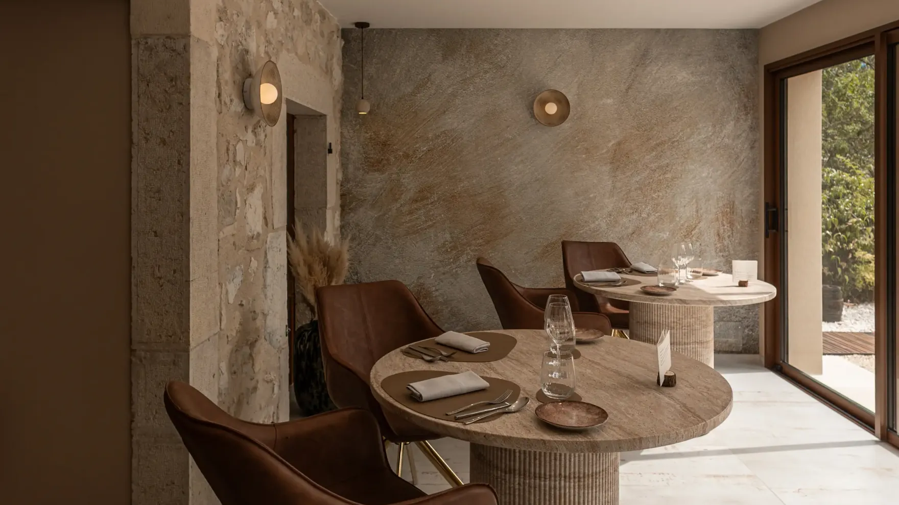 Salle à manger intérieure avec tables rondes en pierre, chaises en cuir brun et murs en pierre apparente