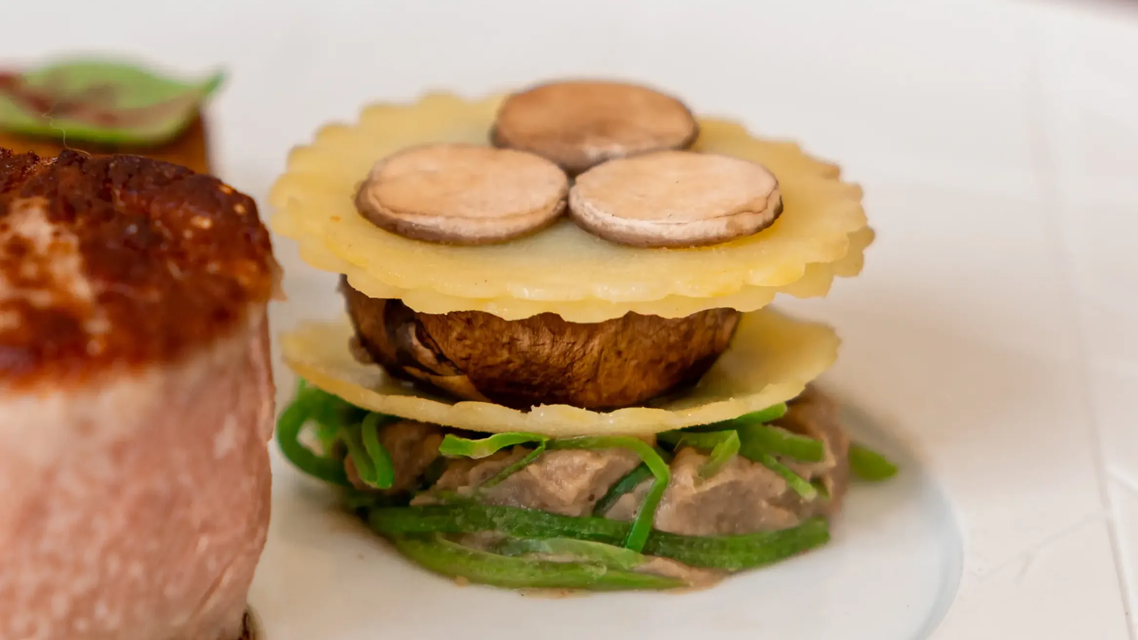 Un plat composé d'une tranche de viande grillée et d'une tour de légumes et de fines tranches de fromage sur une assiette blanche