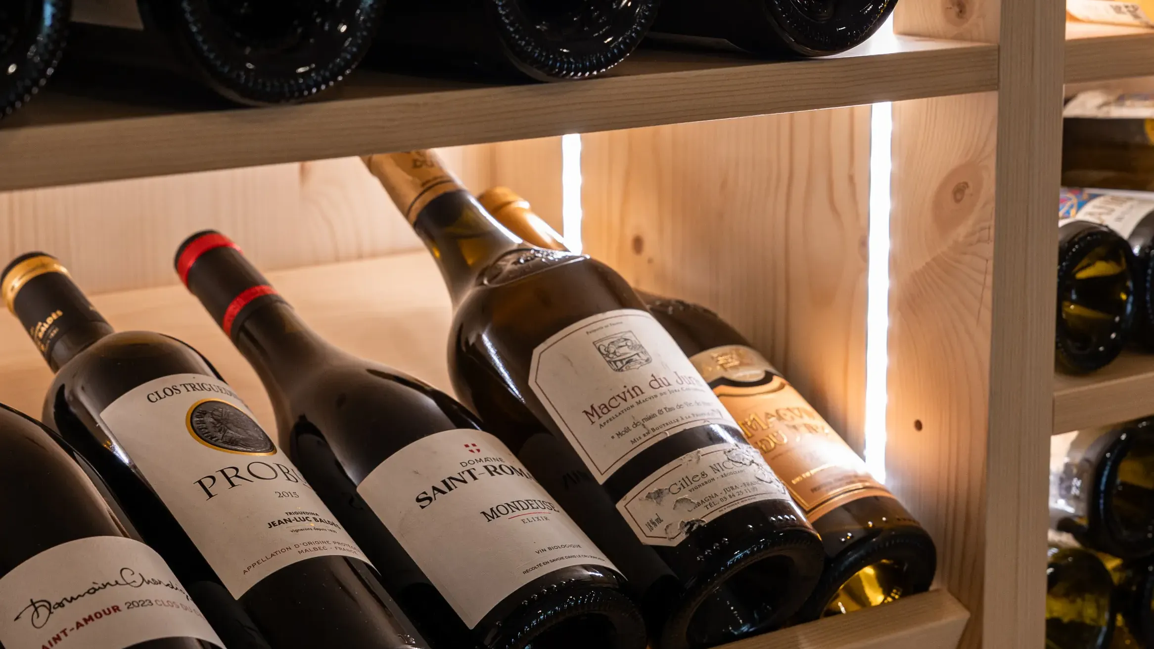 Des bouteilles de vin sont rangées sur des étagères en bois avec des verres à vin posés sur l'étagère supérieure