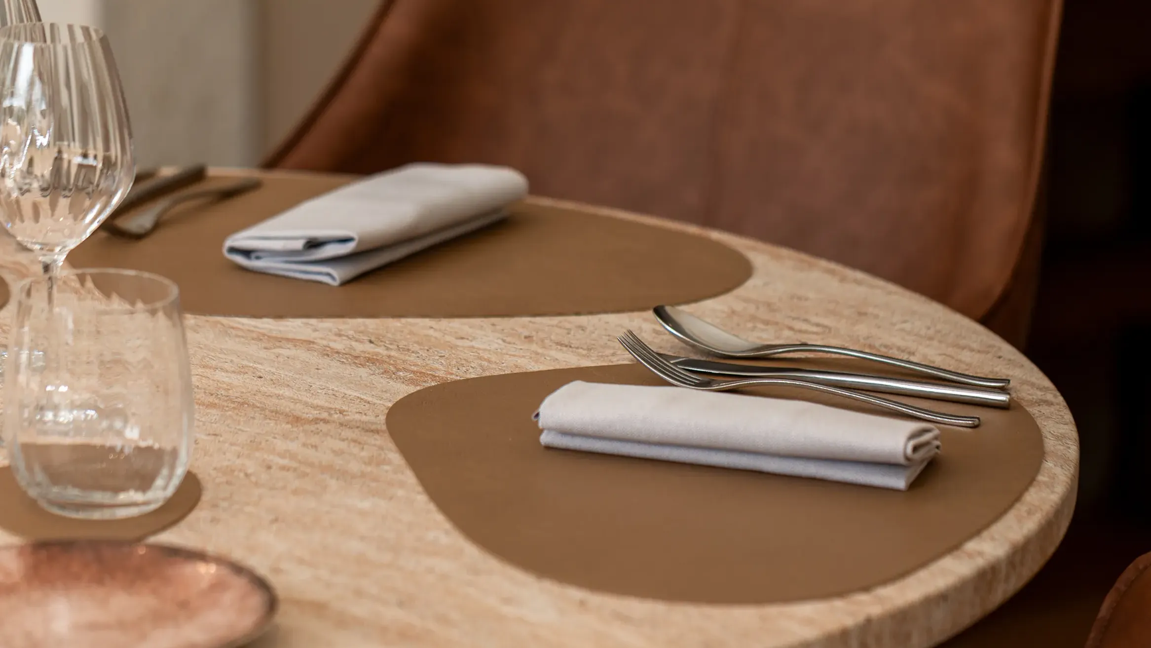 Table ronde en marbre avec des couverts, des verres et des serviettes posés sur des sets en cuir, entourée de chaises en cuir brun